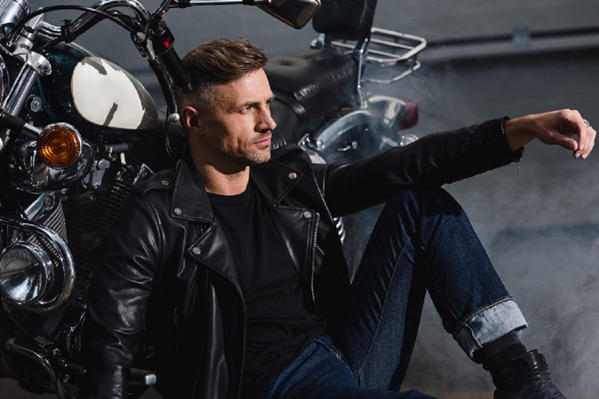 Biker in leather jacket relaxing by motorcycle in garage